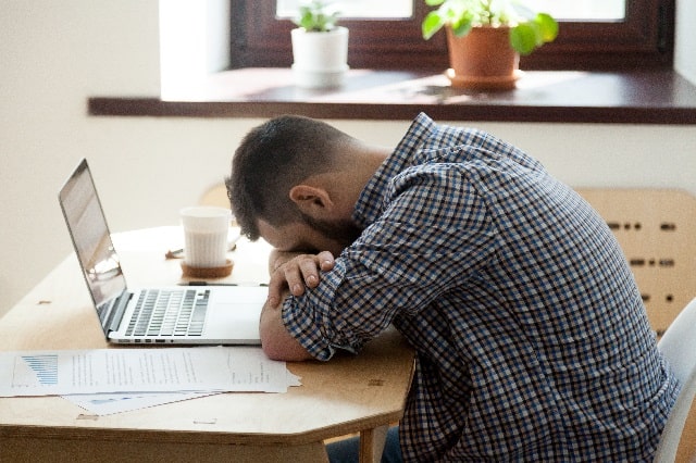 テーブルでパソコンをひらいたまま腕に顔をうずめて寝てしまう男性