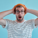 オレンジの帽子で頭を押さえながら口を開けている男性