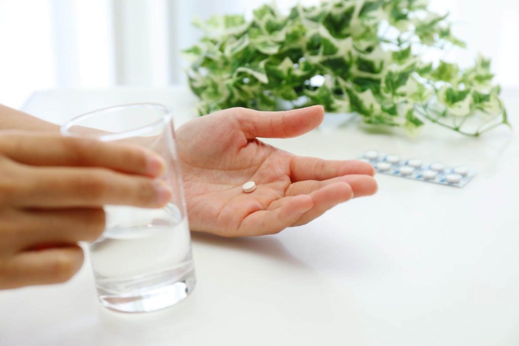 手に薬と水が入ったコップと薬を持つ男性